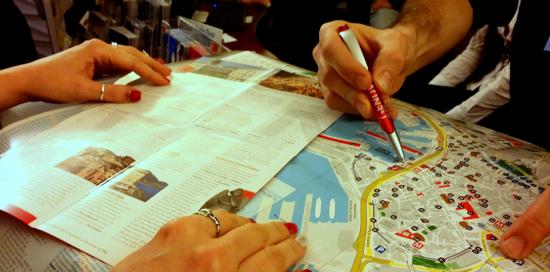 Mani di un turista e di un operatore IAT appoggiate su di una cartina di Genova