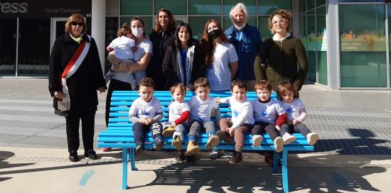 foto di gruppo con bimbi seduti sulla panchina azzurra e autorità dietro in piedi