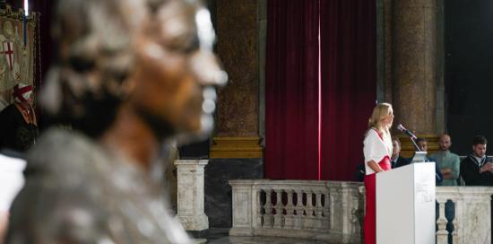 In primo piano un busto di Colombo durante la cerimonia: sullo sfondo, l'intervento della sindaca Salis 