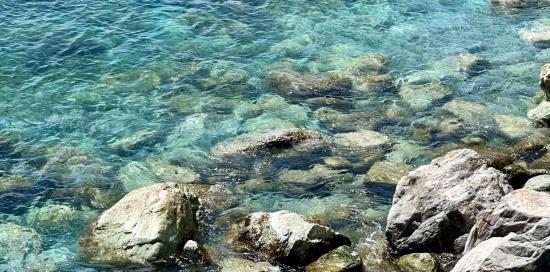 Acqua di mare limpida a bagnare alcuni scogli in primo piano