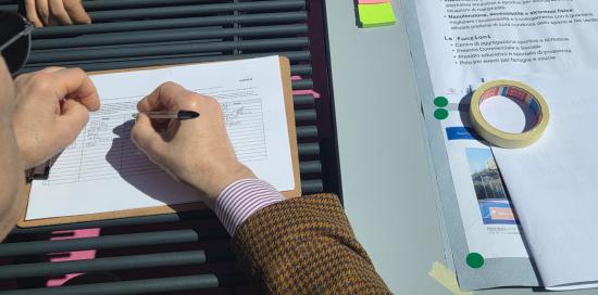 Un partecipante lascia i suoi dati; a destra un foglio con tutte le info sul progetto "Fuori dal Comune"