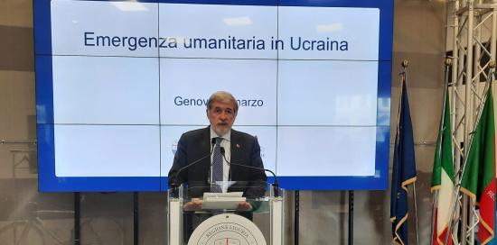 il Sindaco Bucci parla davanti a scritta Emergenza umanitaria in Ucraina