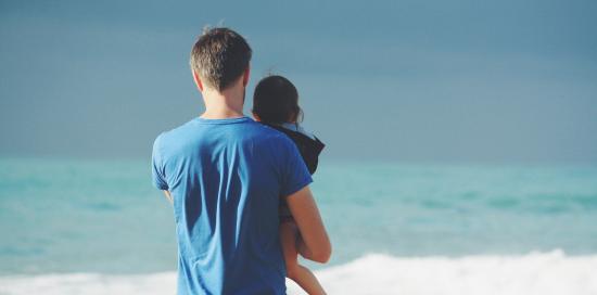 papà con bambino in braccio davanti al mare