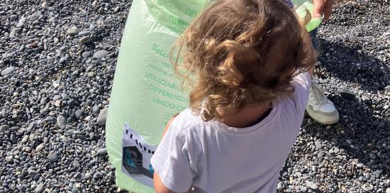 Una bimba, fotografata di spalle, mentre deposita un piccolo rifiuto in un sacchetto tenuto da un adulto - foto di repertorio