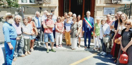 Foto di gruppo davanti al portone di via Strozzi 23 e accanto alla targa: Autorità, relatori, cittadine e cittadini