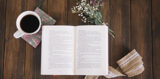 libro aperto, tazza di caffè e fiori su piano in legno