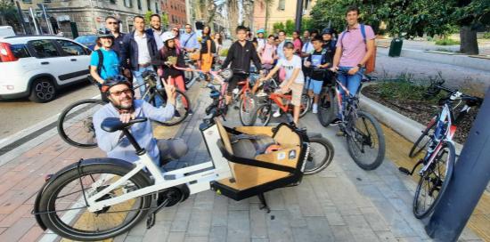 bicibus bambini e genitori: in primo piano cargo-bike per trasporto zaino e casco