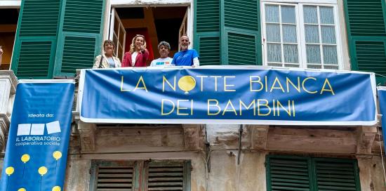 Lo striscione blu "La notte bianca dei bambini" appeso a un terrazzino con Salis, Lodi e organizzatori