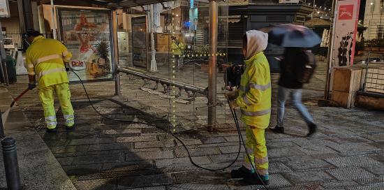 Operatori di Amiu impegnati nella pulizia del marciapiedi di una fermata AMT con l'impiego di una idropulitrice