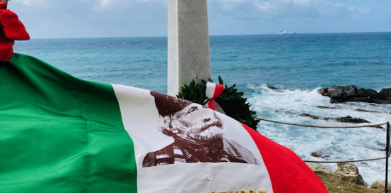 bandiera piegata dal vento davanti alla stele con immagine di Garibaldi