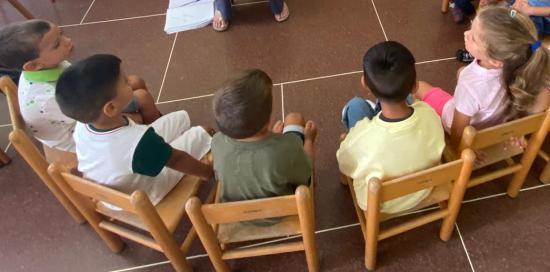 Bimbe e bimbi seduti su piccole sedie e fotografati di spalle