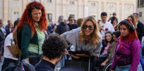 La sindaca Salis saluta un ragazzo sulla carrozzina. Accanto a lei la presidente di Municipio Simona Cosso