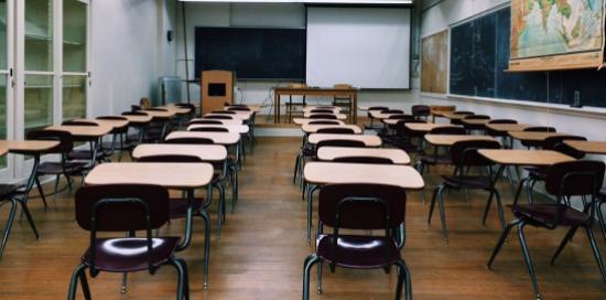Una classe scolastica con tre file ordinate di banchi e sedie, e in fondo la lavagna