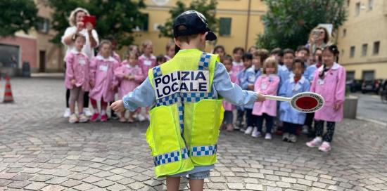 bambino di spalle con paletta e gilet giallo dìcon scritta polizia locale