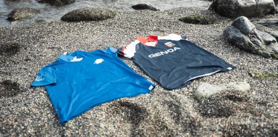 Le magliette in plastica riciclata di Sampdoria e Genoa appoggiate sulla sabbia. Sullo sfondo il mare