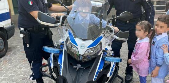 bambino a cavalcioni sulla moto e due vigili motociclisti