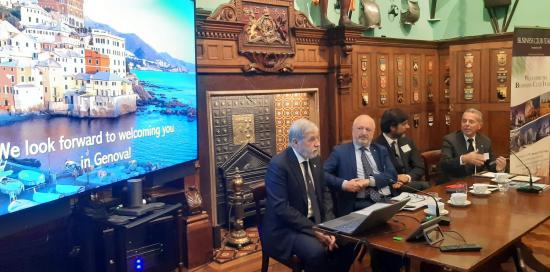 Il sindaco Bucci accanto a uno schermo dove appare una scritta che invita gli astanti a venire a visitare Genova