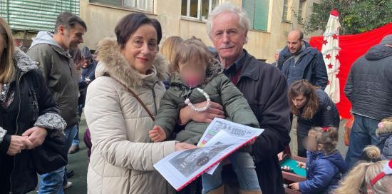 Una coppia di nonni con in braccio la nipotina e in mano calendario e giornalino scolastico