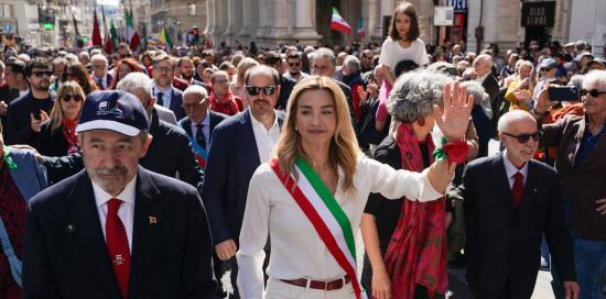 La sindaca Salis saluta i presenti in via XX Settembre durante il corteo: alla sua destra il presidente Bucci