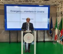 il Sindaco Bucci parla davanti a scritta Emergenza umanitaria in Ucraina