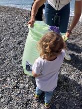 Una bimba, fotografata di spalle, mentre deposita un piccolo rifiuto in un sacchetto tenuto da un adulto - foto di repertorio