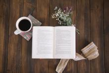 libro aperto, tazza di caffè e fiori su piano in legno