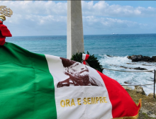 bandiera piegata dal vento davanti alla stele con immagine di Garibaldi