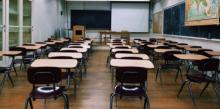 Una classe scolastica con tre file ordinate di banchi e sedie, e in fondo la lavagna