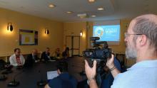 Un cameraman al lavoro durante la conferenza stampa mentre riprende i vari relatori raccolti attorno al tavolo