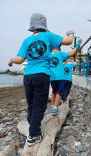 Bimbe e bimbi che "giocano" camminando su un tronco di legno trasportato sulla spiaggia dal mare